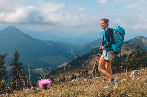 Franziska wandert über eine Blumenwiese im Chiemgau, Bergkulisse im Hintergrund.